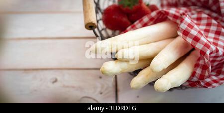 Bundle of seasonal white asparagus in a basket with fresh strawberries. Horizontal background for seasonal gastronomy and healthy nutrition. Close-up. Stock Photo