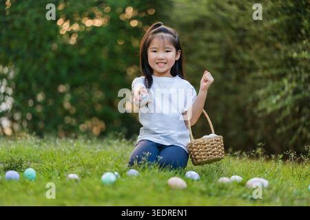 happy child girl playing and hunting for Easter eggs into a basket on green grass in the garden Stock Photo