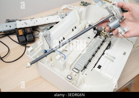 Handheld printer roller and motor above an open, disassembled printer on a desk, depicting repair, maintenance and parts replacement by a technician i Stock Photo