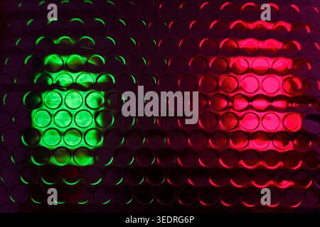 Glossy bubble wrap lit by green and red neon light creates an abstract textured pattern ideal for backgrounds, packaging design concepts, close-up tex Stock Photo