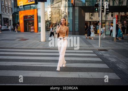 Young woman confidently talking on phone crossing Vienna street Stock Photo