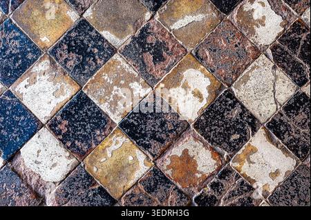 Close-up view of weathered stone floor tiles arranged in a diagonal checkerboard pattern with black, brown, and light-colored squares. The surface of Stock Photo
