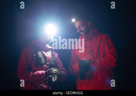 Couple Hikers Wearing Headlamps Checking GPS at Night During Cold Outdoor Adventure Stock Photo