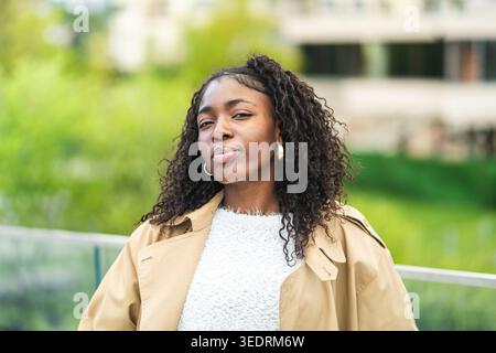 Confident fashionable african american young woman in fancy clothing posing at camera outdoors. Stock Photo
