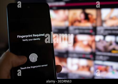 Person holding a smartphone displaying identity verification message for fingerprint authentication, indicating adult content restriction to ensure age verification and digital security Stock Photo