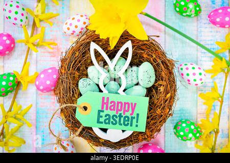 Easter bunny in Easter nest with Easter eggs and label with Easter greeting happy Easter, photomontage Stock Photo