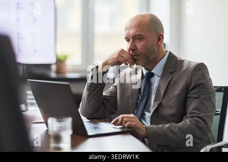 Adult businessman working on laptop, thinking through problem during office analysis and decision making. Ideal for business strategy, leadership, productivity themes Stock Photo