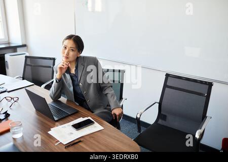 Portrait of Asian young businesswoman sitting at meeting table, working on laptop and planning strategy in office. Ideal for leadership, corporate communication, career growth Stock Photo