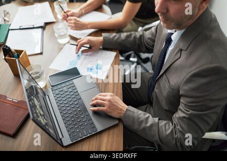 High angle view of adult businessman using laptop during team meeting, analyzing performance data. Ideal for business strategy, finance, reporting themes Stock Photo