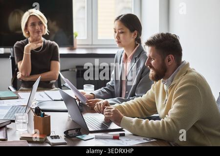 Business team reviewing documents and working on laptops during office meeting, discussing strategy and collaboration. Useful for corporate communication, teamwork or planning campaigns Stock Photo