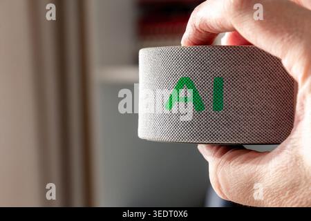Close-up of a hand holding a smart speaker with glowing green AI letters. Concept of artificial intelligence, voice assistant, and smart home tech Stock Photo