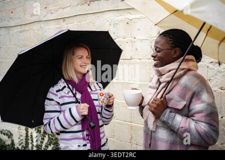 Diverse women friends laughing holding umbrellas drinking coffee Stock Photo