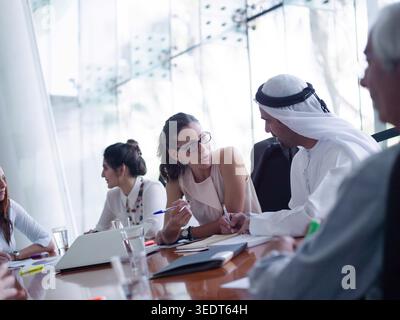 Middle Eastern modern corporate and startup professionals collaborate in a bright glass boardroom, exchanging notes and ideas during a focused business meeting. Diverse team members discuss strategy, planning and partnership. Stock Photo