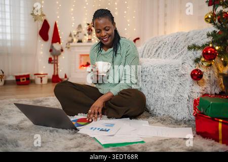 Woman analyzing documents and using laptop at home during Christmas Stock Photo