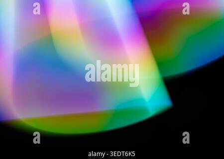 Gentle colorful light leaks with a dreamy bokeh effect. Vibrant prism refractions create soft, glowing shapes and fluid gradients on a black surface, perfect for artistic backgrounds. Stock Photo