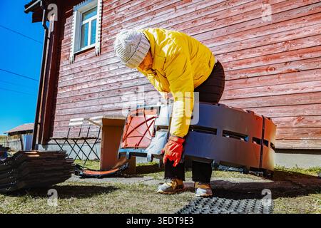 Interlocking compost bin panels being connected into circular structure by woman near country home. Stock Photo