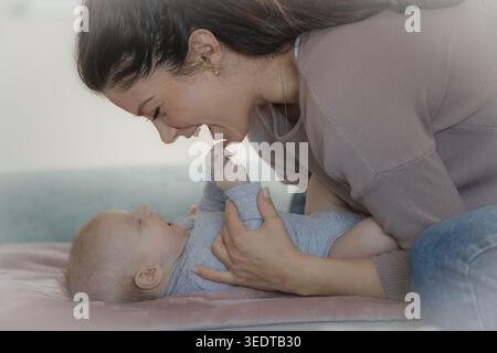 Cute newborn baby lying on back and smiling at mother on bed at home Stock Photo