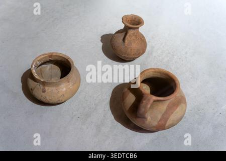 Ancient handmade clay pottery on light background. Three terracotta vessels: two pots and one small jug with painted stripes. Archaeological artifacts Stock Photo