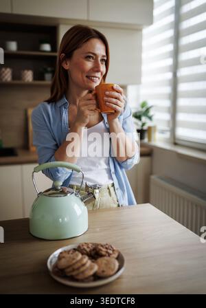 A woman stands by a table in a kitchen, preparing kholodets, aspic, or ...