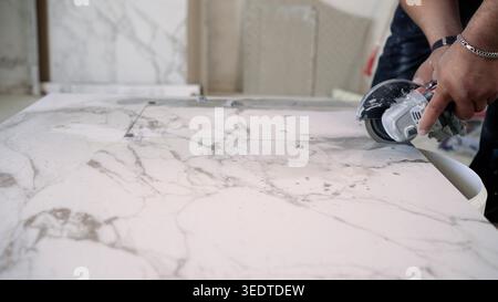 A worker uses an angle grinder with a diamond blade to cut a rectangular hole in a large marble-patterned porcelain tile. Close-up on hands and tool d Stock Photo