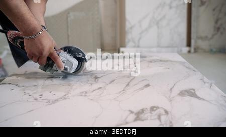 A construction worker uses an angle grinder to cut a large white marble or porcelain tile. Close up shot of hands guiding power tool along a straight Stock Photo