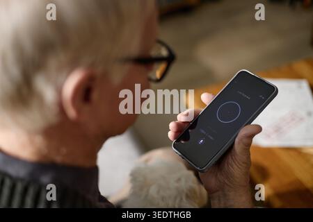 Senior Man Using Smartphone Voice Assistant at Home Stock Photo