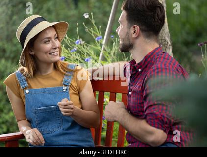Pretty woman gazing lovingly at her partner as he's talking while taking a break on bench after gardening work Stock Photo