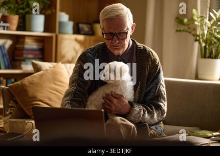 Senior Man Holding Dog While Using Laptop for Remote Communication Stock Photo