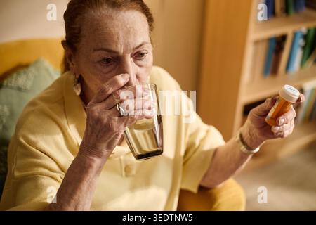 Senior Woman Taking Medication with Water at Home Stock Photo