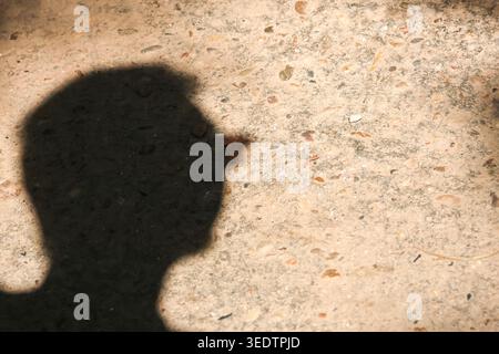 Dark shadow of contemplative person with glasses forming silhouette on rough concrete surface creating an abstract texture and sense of deep mystery Stock Photo
