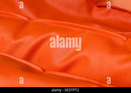 Close macro shot capturing folded bright orange leather texture creating vibrant inviting background surface highlighting premium soft fabric material Stock Photo