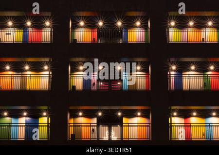 Close view of a modern facade with colorful window panels and starburst lights creating a repeating geometric pattern at night. Stock Photo