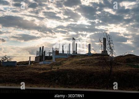Dramatic sunset over old cemetery with ancient stone stelae and burial mounds on a hill. Bright sun rays breaking through dramatic clouds create power Stock Photo