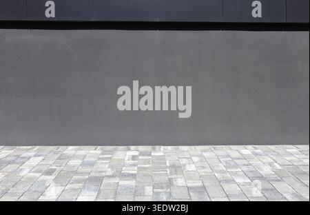 Gray plaster wall  with yard in front made of concrete paver tiles . Background for copy space, add text. Stock Photo