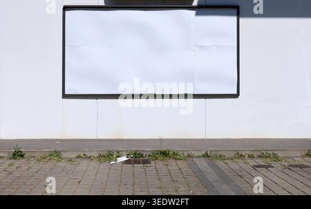 Blank street billboard at roadside on white prefab concrete wall. Dirty sidewalk and tiled street in front. Background for copy space, add text. Stock Photo