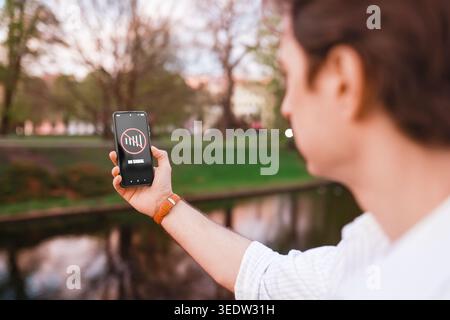Man holding a smartphone with a "No Signal" warning icon while standing in a park. Concept of weak cellular network, internet connection failure, and Stock Photo