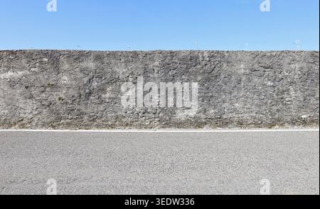 Rough boundary concrete surrounding wall under a blue sky with a row of tv antennas far behind.  Street in front. Background for copy space, add text. Stock Photo