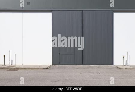 Sliding industrial door (or side-folding) made of dark gray metal with an integrated pedestrian door. Background and texture. Stock Photo