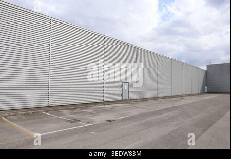 Large corrugated aluminum cladding wall with empty parking lot in front. Cloudy sky above. Background and texture, copy space Stock Photo