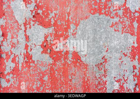 Distressed metal surface with peeling red paint and rough gray textured background. Stock Photo