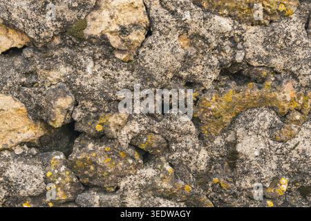 Aged stone wall surface with rough rocks, cracks, and yellow moss details. Stock Photo