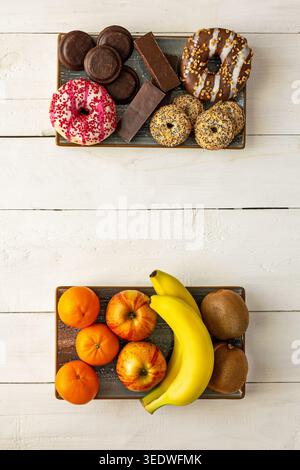 Healthy Fruit Plate Versus Sweet Desserts. Overhead view of fruit and dessert trays comparing healthy snacks with donuts, cookies, chocolate bars and Stock Photo