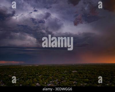Wide aerial drone view of dark stormy clouds over a lush green suburban neighborhood at sunset in Naperville Illinois during the spring season Stock Photo