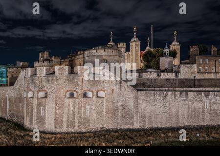 Night view of the historic Tower of London fortress under a dark, cloudy sky Stock Photo