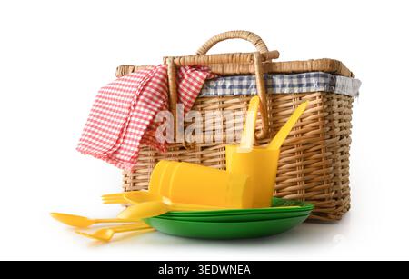 Wicker picnic basket with yellow plastic plates, cups, cutlery and red checkered cloth isolated on white background. Stock Photo