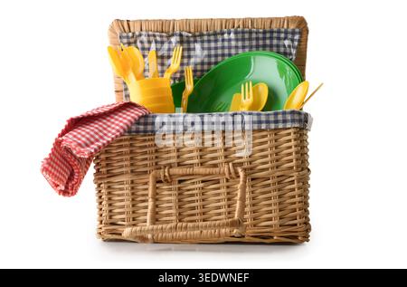 Open wicker picnic basket filled with colorful plastic dishes and cutlery, isolated on a white background. Stock Photo