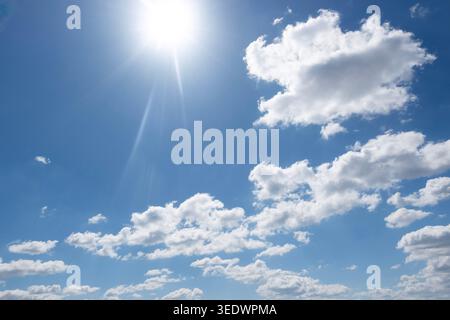 Bright sun shining in blue sky with white fluffy clouds, clear summer weather background Stock Photo