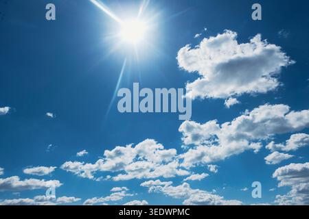 Bright sun shining in blue sky with white fluffy clouds, clear summer weather background Stock Photo