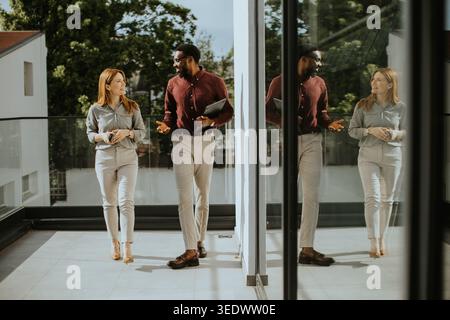Two professionals walk on a balcony discussing business plans. They share ideas while enjoying the bright afternoon light. The setting is modern and r Stock Photo