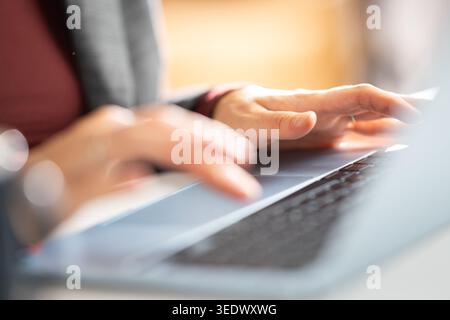 Person types on a laptop at a workspace while focused on tasks during the daytime in a bright environment Stock Photo